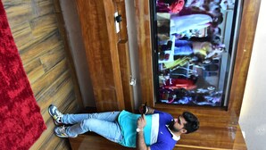 A person standing in a room with a wooden floor, a red rug, and a television displaying a crowd. - Hotel M2M  Narela (New Delhi)