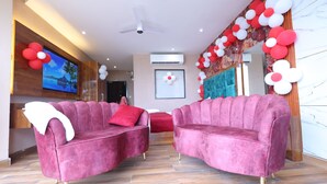 A modern hotel lobby with two pink sofas, a ceiling fan, a TV, and red and white balloon decorations. - Hotel M2M  Narela (New Delhi)