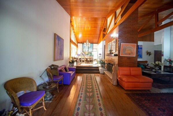 A spacious living room with a wooden ceiling, a fireplace, and a dining area in the background. - Hotel Colinas de Petropolis (Petrópolis)
