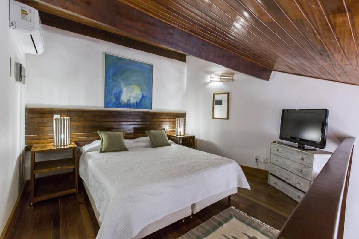A bedroom with a wooden headboard, a bed with white bedding, a television on a dresser, and a painting on the wall.