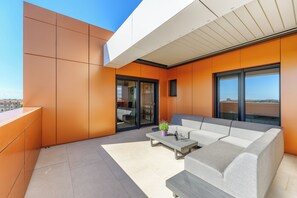A modern outdoor living area with a grey sofa, a small table with a plant, and large windows offering a view of the cityscape. - Luxury Penthouse Viki with sea view (Umag)