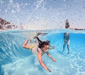 An underwater view of a swimming pool with clear water, a child swimming, and another person in the background. - Biebosch - Sunshower (Valkenburg)