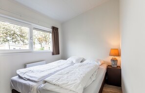 A bedroom with a bed, a window, a radiator, and a nightstand with a lamp. - Biebosch - Sunshower (Valkenburg)