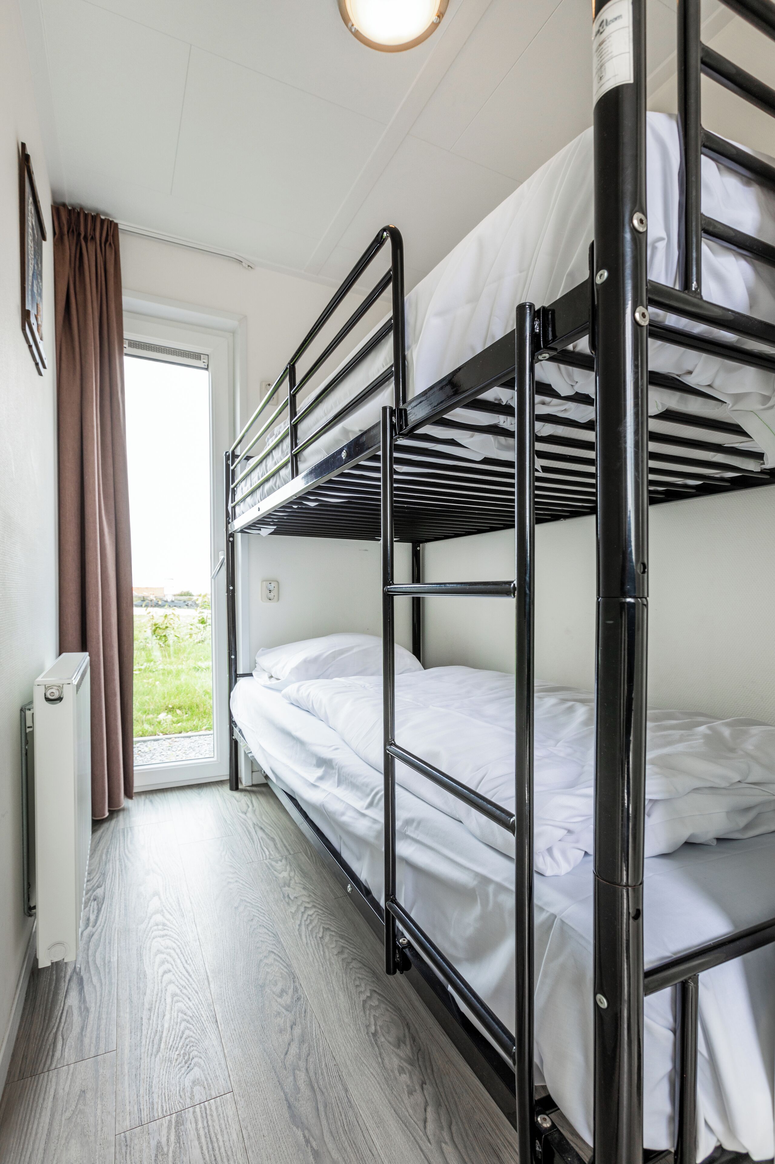 A bunk bed room with a window, a radiator, and a door.