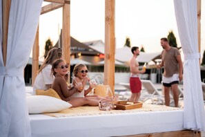 A wooden deck with a bed, a tray with items, and a pool area in the background.