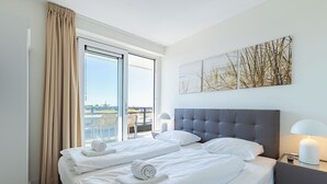 A hotel room with a large bed, two bedside tables, a window with curtains, and artwork on the wall.