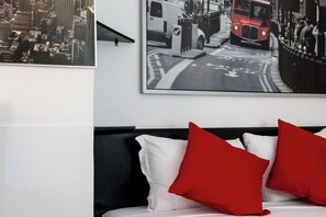 Ein Schlafzimmer mit einem Bett, weißen und roten Kissen, einem schwarzen Kopfteil und einem Stadtlandschaftsbild an der Wand.