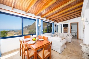 A dining area with a table set for four, a sofa, and a view of the sea.