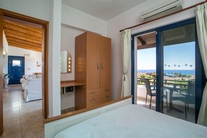 A bedroom with a large bed, a wardrobe, a desk, and a view of the sea.