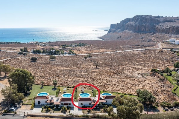 Una zona costera amb un grup de cases que tenen piscines, envoltades d'un paisatge àrid i un penya-segat.