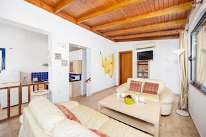 Una sala de estar con un sofá, una mesa de centro con fruta, un televisor y una cocina con armarios y microondas.