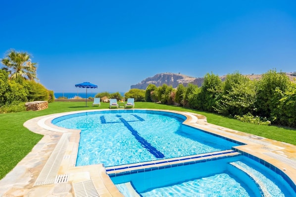 Una piscina con un cielo azul despejado, una montaña al fondo y un césped bien cuidado.