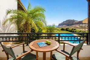 Une table en bois, entourée de chaises, sur un balcon, d’où l’on peut admirer une piscine et un paysage montagneux.