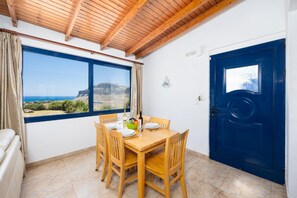 A dining area with a table set for four, a view of the sea, and a blue door.