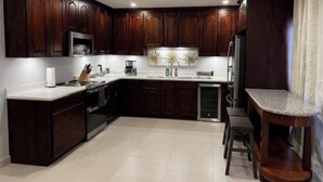 Una cocina moderna con armarios de madera oscura, encimera blanca, microondas integrado y refrigerador de acero inoxidable.
