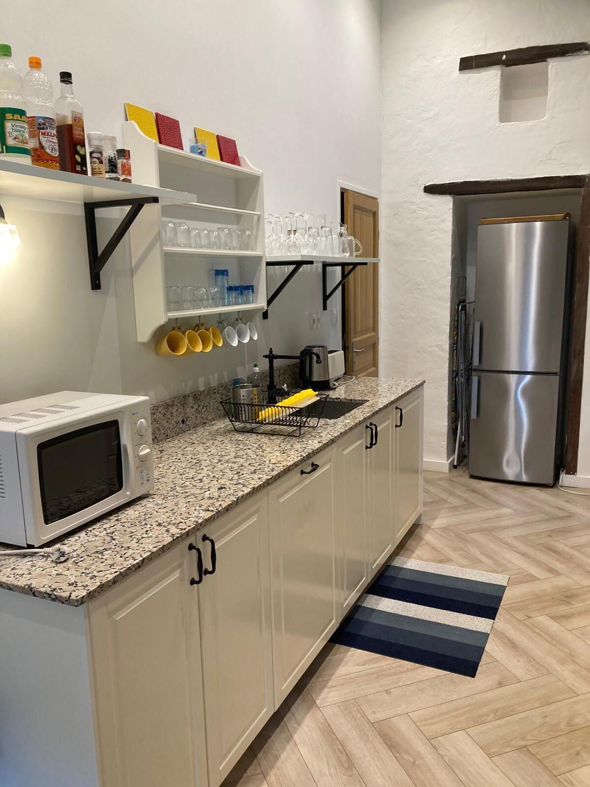 Eine Küche mit Mikrowelle, Edelstahlkühlschrank und einem Regal voller Küchenutensilien.