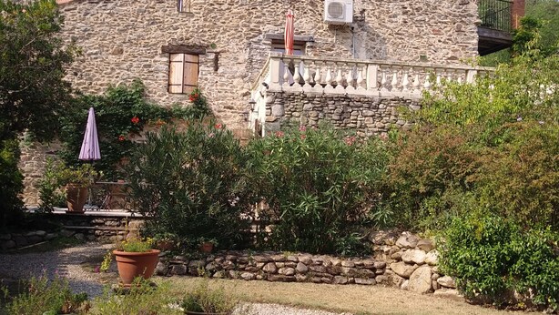 A stone building with a balcony, potted plants, and a gravel pathway.