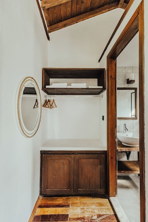 A bathroom with a wooden vanity, a mirror, and a shelf above the sink.