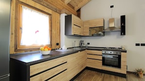 A modern kitchen with wooden cabinetry, a built-in oven, and a window with a decorative view. - Baita La Ciamorza Near Dolomiti - Veneto (Lozzo di Cadore)