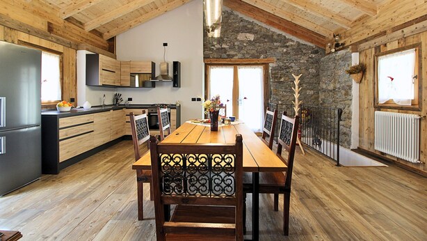 A spacious kitchen with wooden beams, a stone wall, and a dining area with a wooden table and chairs. - Baita La Ciamorza Near Dolomiti - Veneto (Lozzo di Cadore)