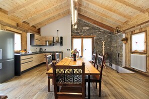 A spacious kitchen with wooden beams, a stone wall, and a dining area with a wooden table and chairs. - Baita La Ciamorza Near Dolomiti - Veneto (Lozzo di Cadore)