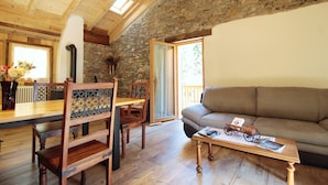 A cozy living room with a stone wall, wooden furniture, and a large window. - Baita La Ciamorza Near Dolomiti - Veneto (Lozzo di Cadore)