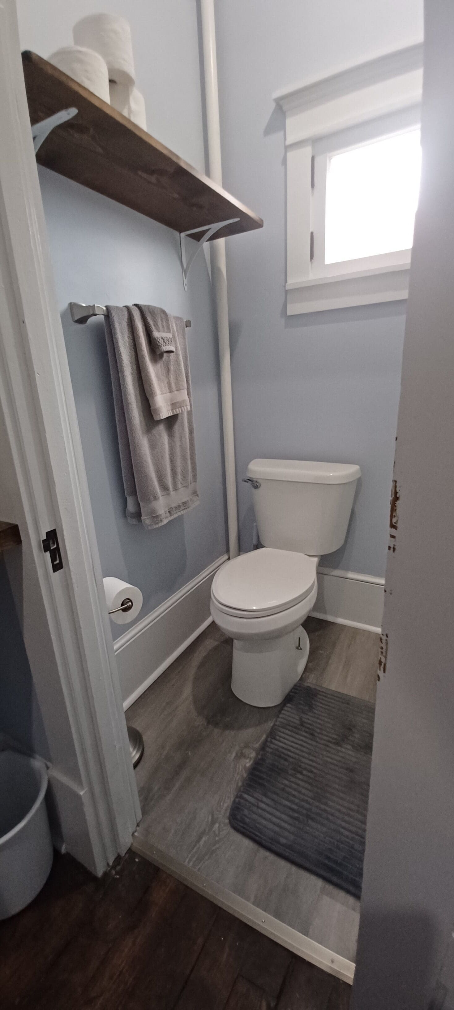 Une salle de bain comprenant des toilettes, un porte-serviettes avec des serviettes, un rouleau de papier toilette et une fenêtre.
