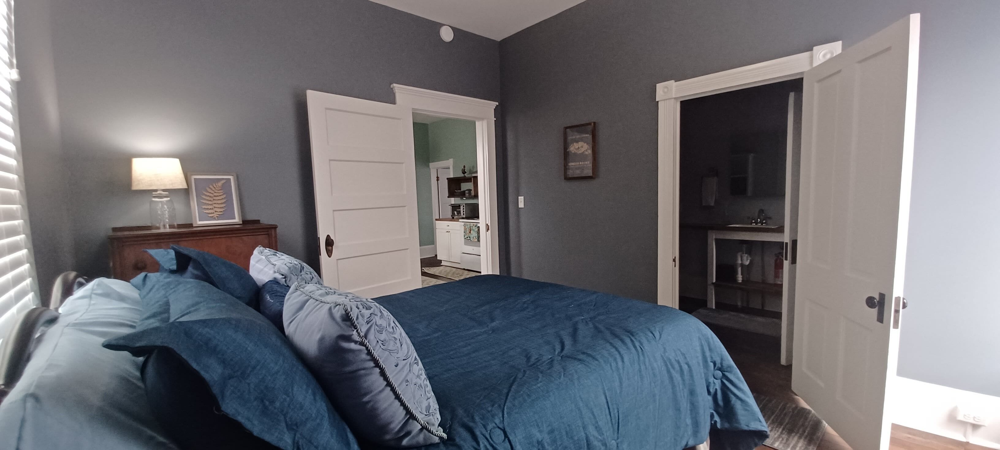 A bedroom with a bed, a nightstand, a lamp, and a door leading to a bathroom.