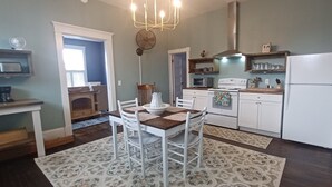 Una cocina con armarios blancos, estufa, microondas y refrigerador. Hay una mesa de comedor con sillas y una araña.