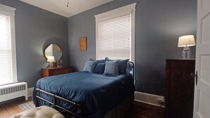 Un dormitorio con cama, cómoda, espejo y radiador.