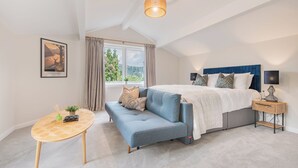 Un dormitorio con cama, un sofá azul, una mesita y una ventana con cortinas.