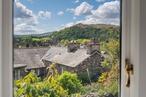 A stone building with a sloped roof, surrounded by greenery and a view of a hill with a church steeple. - Chapel Lodge - Central Ambleside (Ambleside)