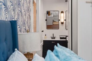 A bedroom with a bed, a bedside lamp, a nightstand, and a bathroom visible through an open door. - Four Bedroom Beach House - Walk to Park and Beach (Isle of Palms)