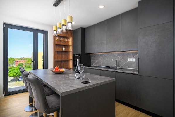 A modern kitchen with a large island, dark cabinetry, and a view through the glass door.