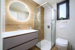 A modern bathroom with a wooden vanity, a glass shower enclosure, and a toilet.