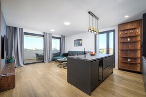 A modern kitchen with a central island, a dining area with a sofa, and a large window offering a city view.