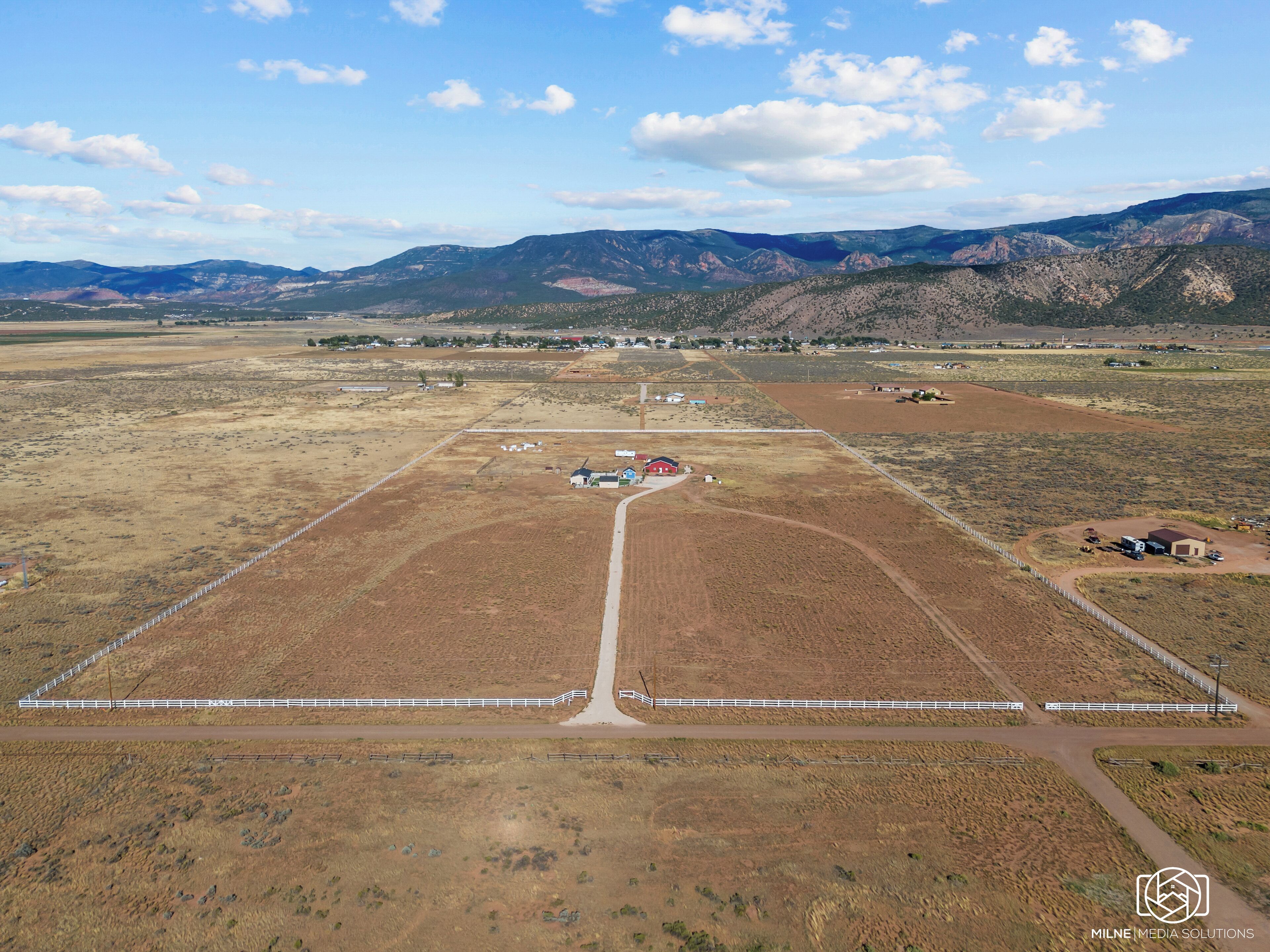 An aerial view of a rural area with fields, a fenced area, and a few buildings.