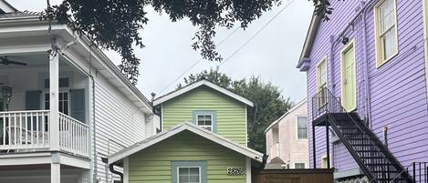 A residential street with houses, including a green house with the number 2826, a white car parked on the street, and a purple house with a black staircase.