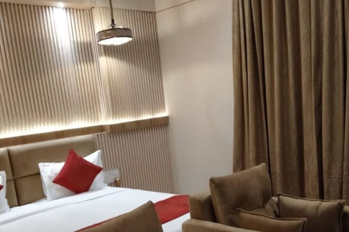 Une chambre d’hôtel avec un grand lit, deux canapés, un plaid rouge et un luminaire au plafond.
