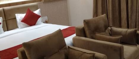 Habitación de hotel con una cama grande, dos sofás, un plaid rojo y una lámpara en el techo.