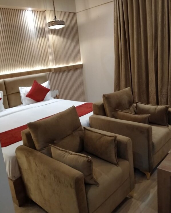 A hotel room with a large bed, two sofas, a red throw, and a ceiling light.