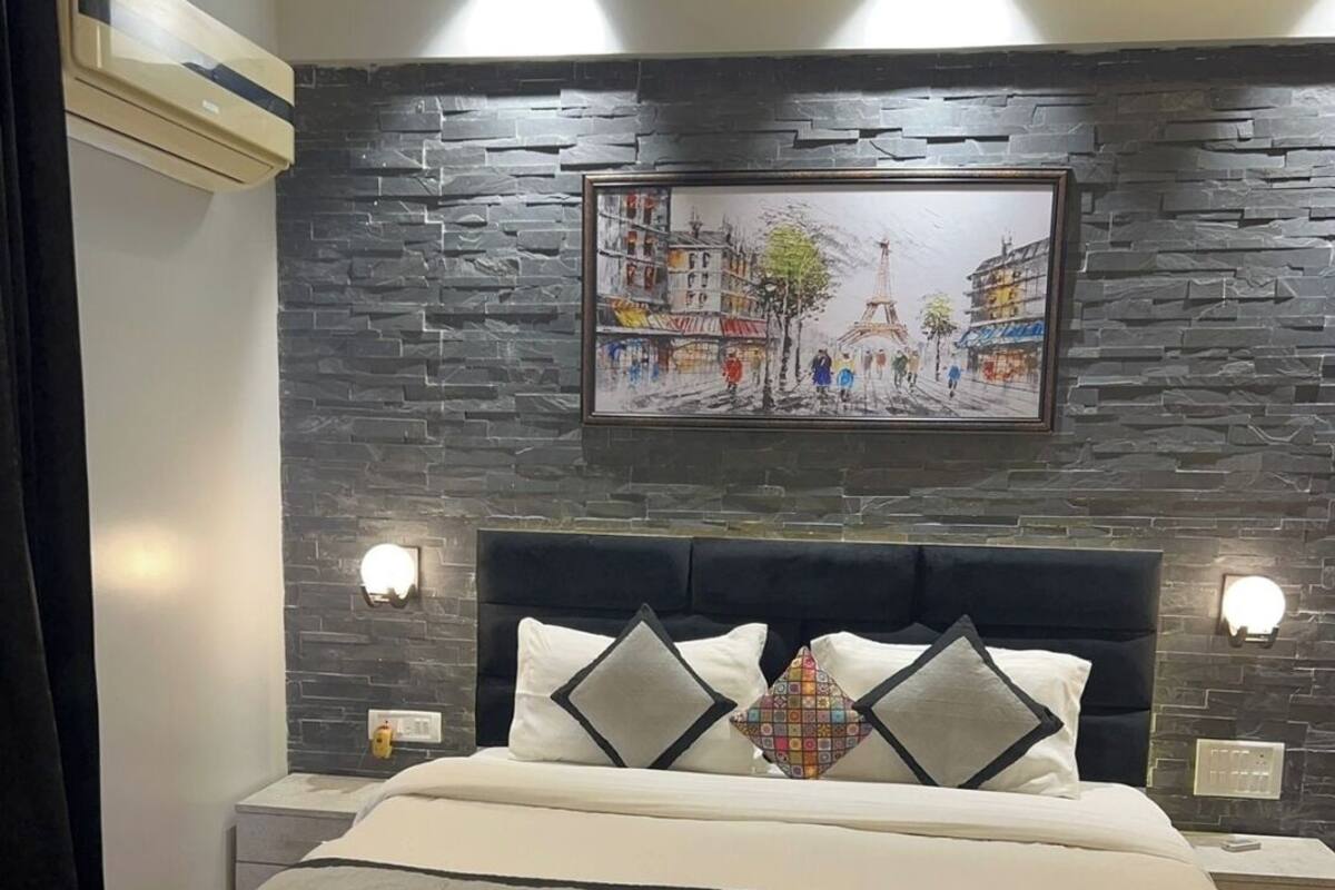 Une chambre moderne avec un mur d’accent en pierre, un grand lit avec une tête de lit noire et deux lampes de chevet.