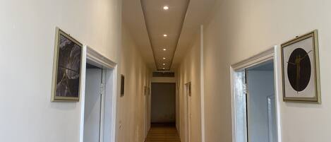 A hallway with wooden flooring, white walls, and doors with framed artwork.