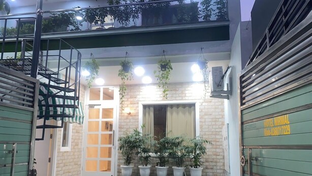 Entrada de hotel con puerta de vidrio, plantas en macetas y toldo verde.