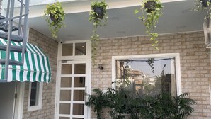 Un edificio de ladrillo con una puerta blanca, una ventana y varias plantas en macetas.