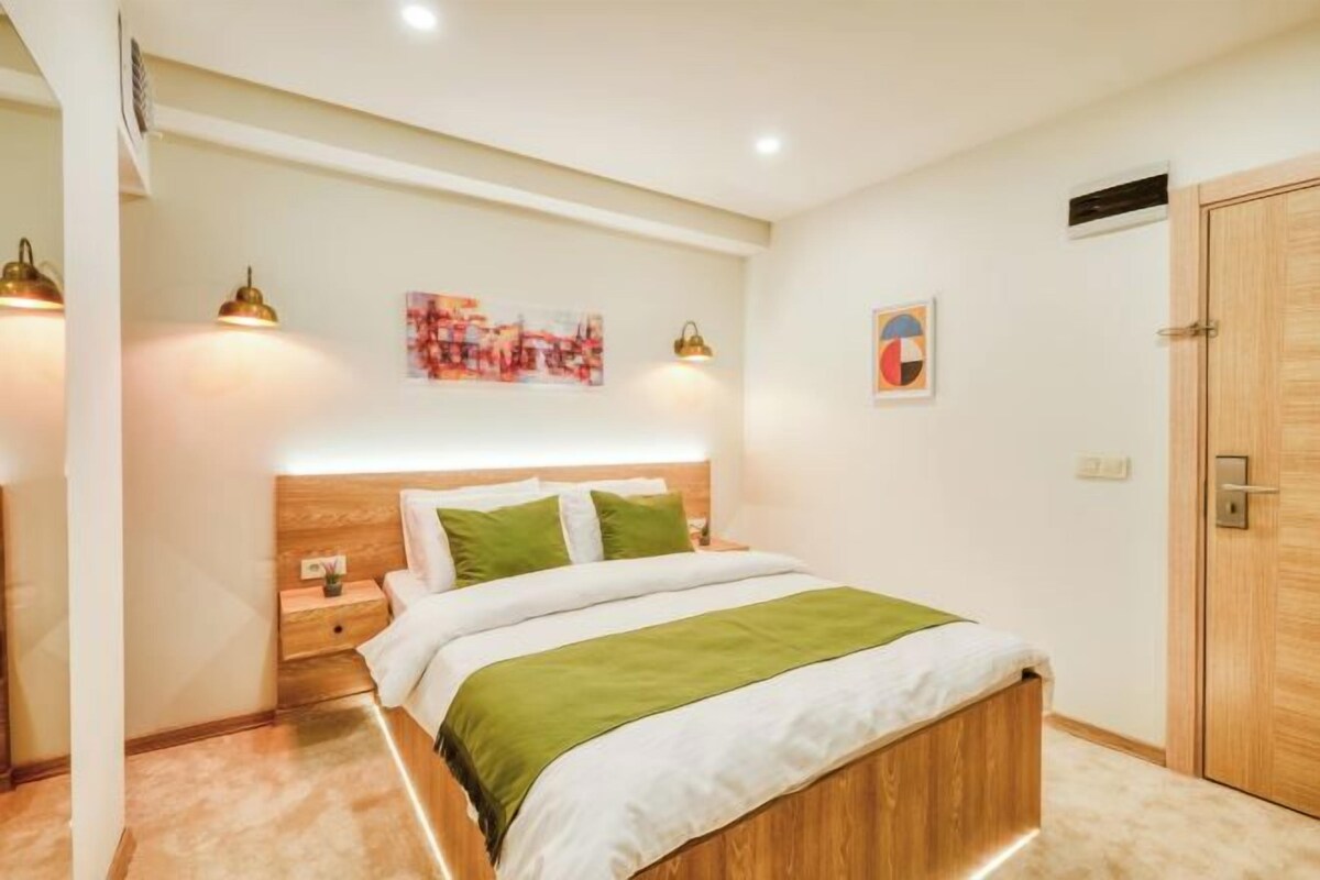 A bedroom with a wooden headboard, a bed with green and white bedding, two bedside lamps, and a wooden door.