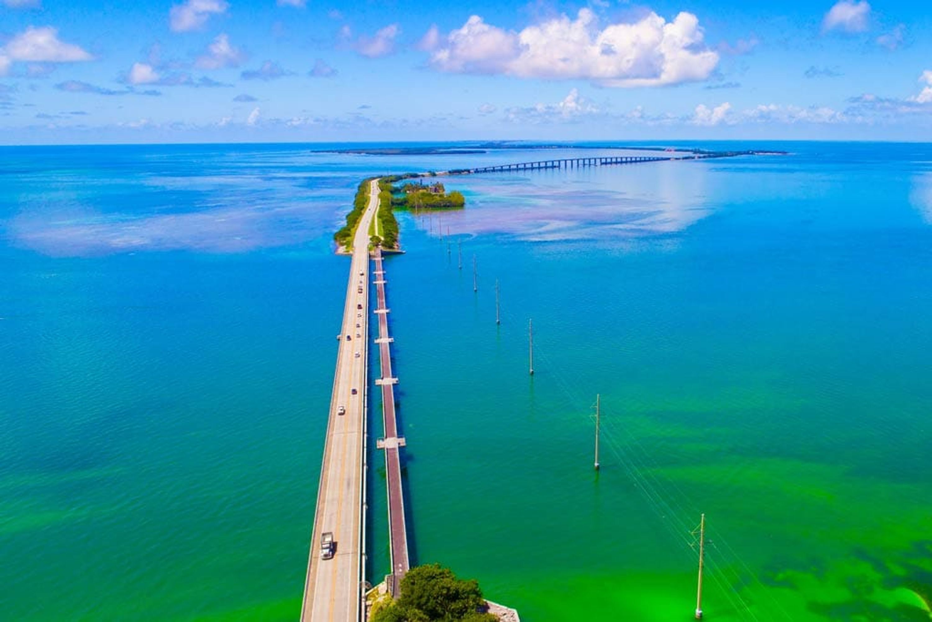 Une vue aérienne d’un long pont qui s’étend au-dessus de l’océan, avec un ciel dégagé.