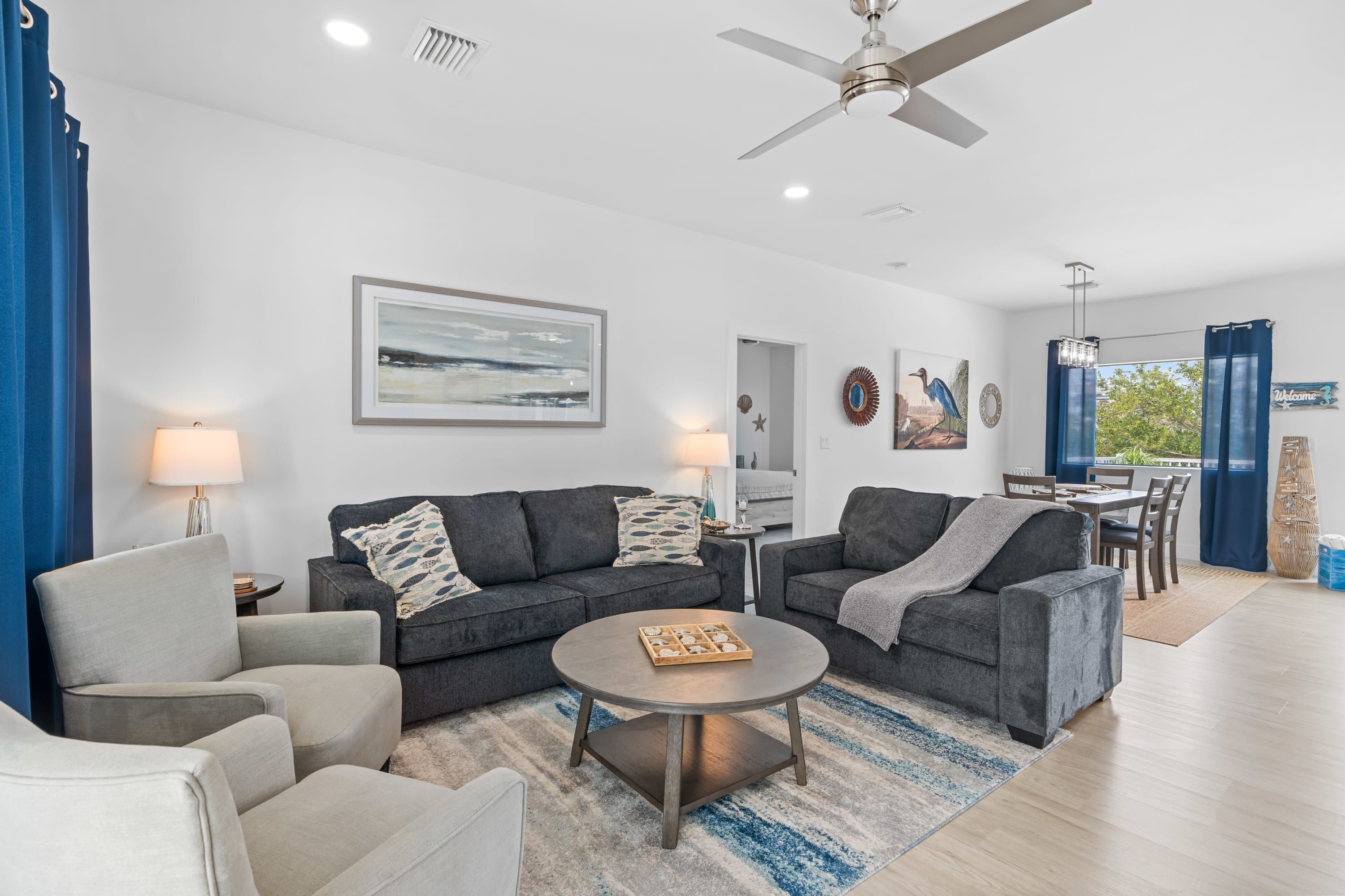 A modern living room with two grey sofas, a round coffee table, and a dining area with a table and chairs.