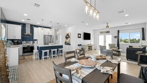 A modern kitchen with white cabinets, a central island, and a dining area with a table set for four. - Blue Pearl Waterfront Oasis w Pool 70 Dock (Marathon)