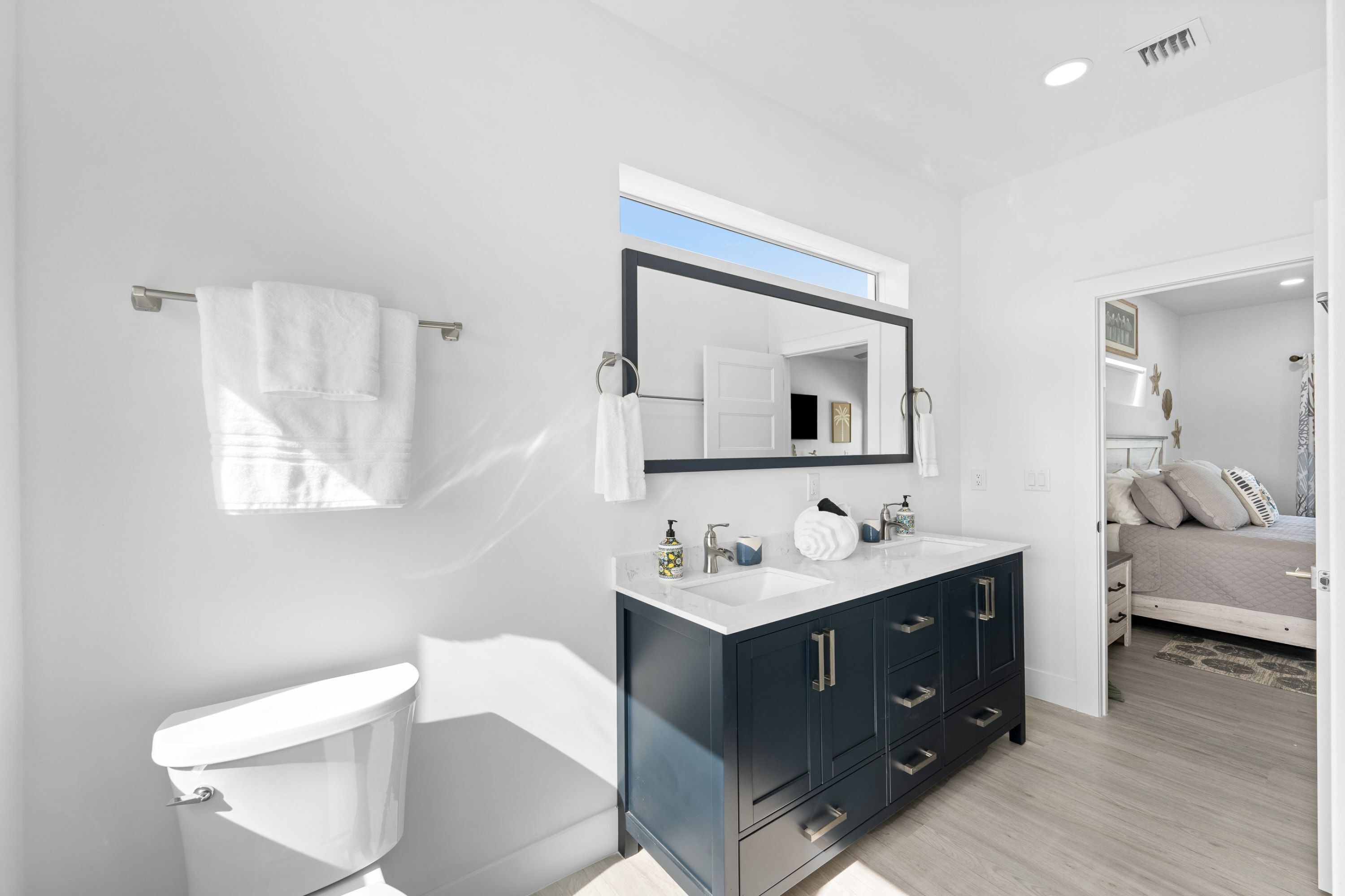 A modern bathroom with a white toilet, a dark vanity with drawers, a large mirror, and a towel hanging on a rack.
